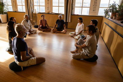 Group of diverse people with instructor sitting on floor and practicing meditation during traditional chi kung session in studio