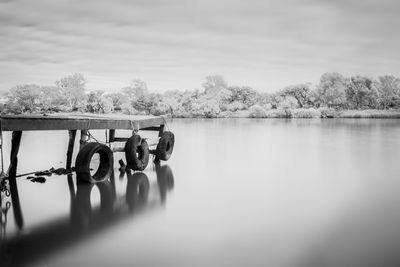 Black and white pier with reflection of trees on river against sky