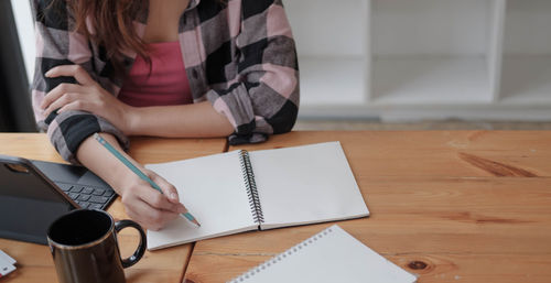 Midsection of woman reading book while sitting on table