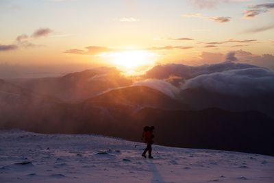 Man standing on snowcapped mountain against sky during sunset