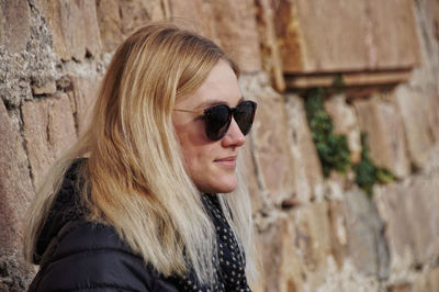 Close-up of woman wearing sunglasses standing against wall
