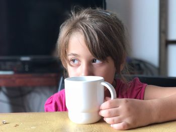 Close-up of girl looking away while holding coffee cup at home