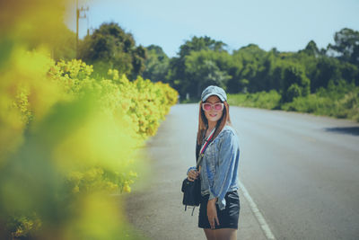 Portrait of beautiful woman wearing sunglasses standing on road side