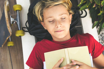 Thoughtful boy with book sleeping on floor in park