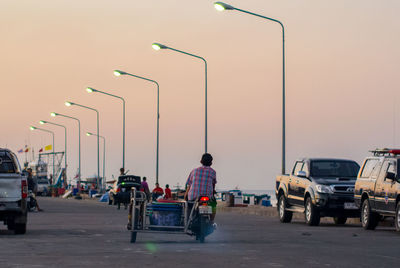 Rear view of man riding motor scooter on street at dusk