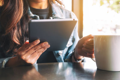 Midsection of woman using digital tablet while sitting at cafe table