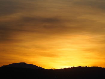 Scenic view of silhouette mountains against dramatic sky during sunset