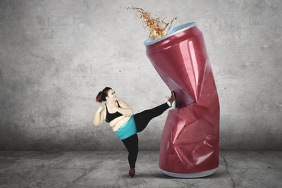 Digital composite image of woman kicking drink can against wall