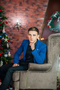 Portrait of young man sitting on sofa at home during christmas celebration