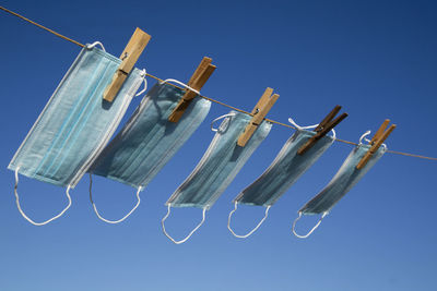 Low angle view of clothespins hanging on rope against blue sky