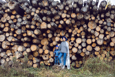 Mom and son are standing by the logs at the sawmill in autumn in warm clothes