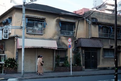 Women walking on sidewalk against houses in city