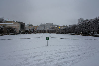 Snow covered field by city against sky