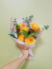 Close-up of hand holding flower bouquet against yellow background