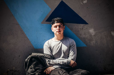 Portrait of young man sitting against wall