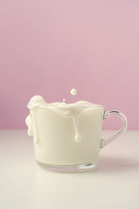 Milk pours out of a transparent cup on a purple background.