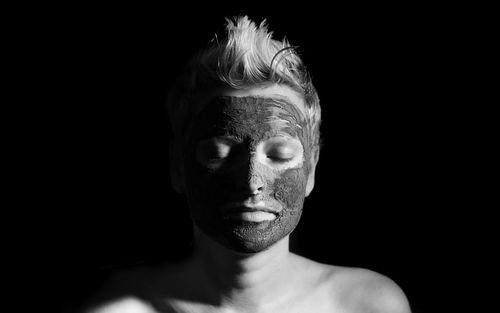 Shirtless woman wearing mask against black background