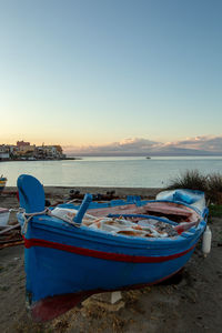 Boat moored on beach against sky during sunset