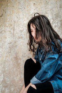 Beautiful young woman sitting against wall