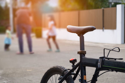 Cropped image of bicycle parked on road while family playing in background