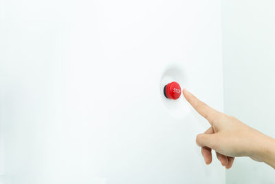 Close-up of hand pressing red button on wall