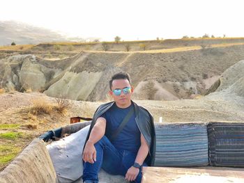 Portrait of man sitting on landscape against sky