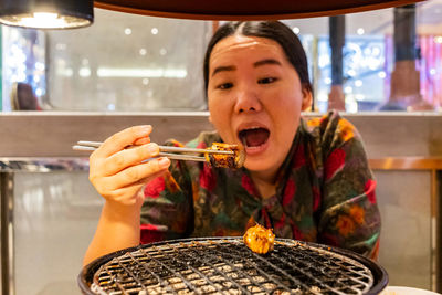 Portrait of woman eating food by barbecue grill in restaurant