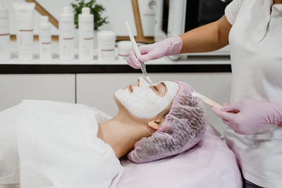 Cosmetologist applying mask on client's face in spa salon. young woman getting facial care 