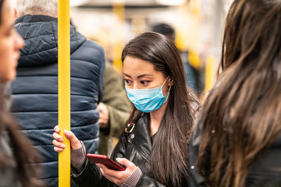 Woman wearing mask using smart phone in subway train