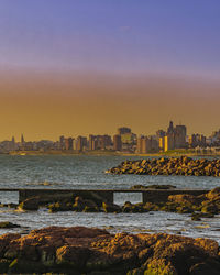 Sea by buildings against sky during sunset