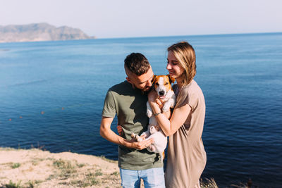 Happy couple with favourite pet. young man and woman have walk near sea.