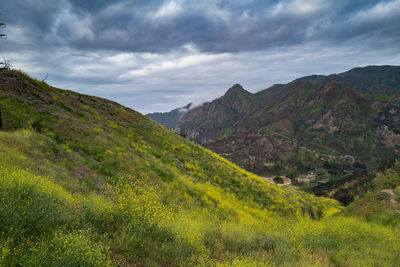 Scenic view of green landscape and mountains against cloudy sky