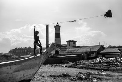 Shirtless boy holding kite while standing on boat against sky