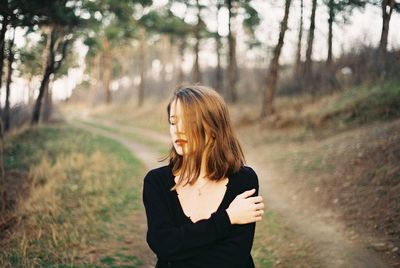 Young woman standing by tree in forest