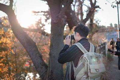 Rear view of man photographing on tree trunk