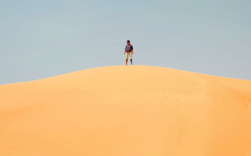 Man standing on sand dune in desert against clear sky