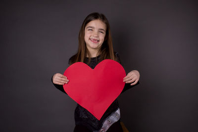 Portrait of smiling girl holding heart shape over black background