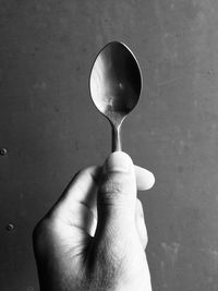 Close-up of hand holding spoon against wall