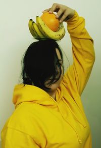 Young woman carrying fruits on head by wall