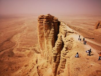 People on rock formations in desert against sky