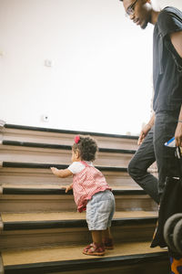 Young man looking at daughter climbing staircase in apartment