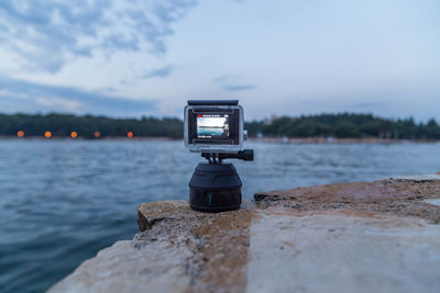 Close-up of camera on rock by sea against sky