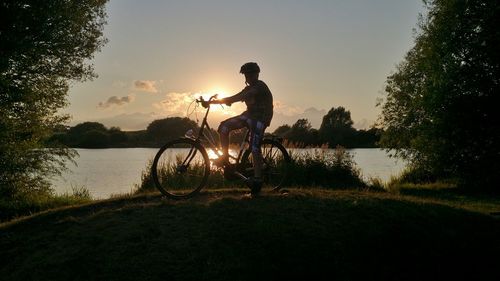 Boy with bicycle on road by lake against sky during sunset