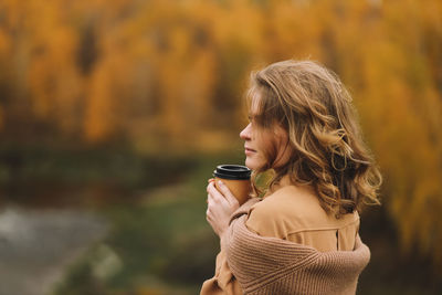 A pretty girl enjoys solitude drinks coffee walks in the autumn forest in nature in fall