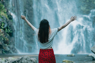 Rear view of woman standing against waterfall