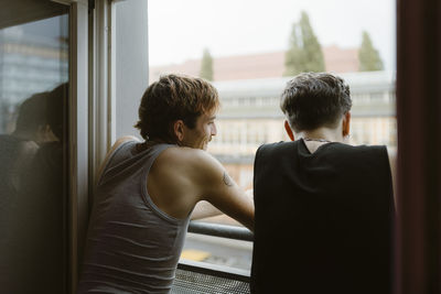 Rear view of gay men looking out of window in apartment