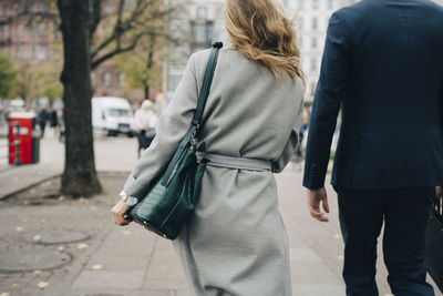 Rear view of businesswoman with handbag walking by colleague in city