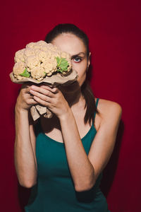 Portrait of woman holding cauliflower against red background