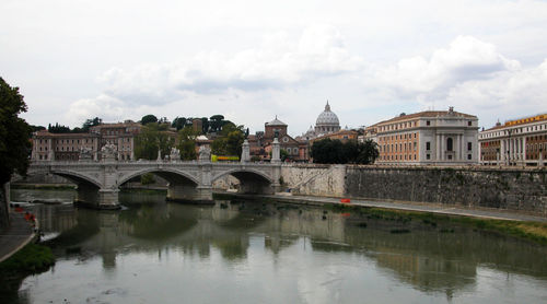 Bridge over river by buildings against sky in city