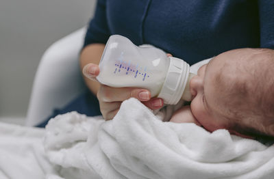 Midsection of mother feeding son with milk bottle